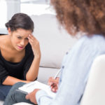 Woman crying on sofa while therapist is taking notes
